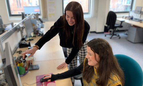 Procurement Apprentice at her desk with a colleague looking at a screen